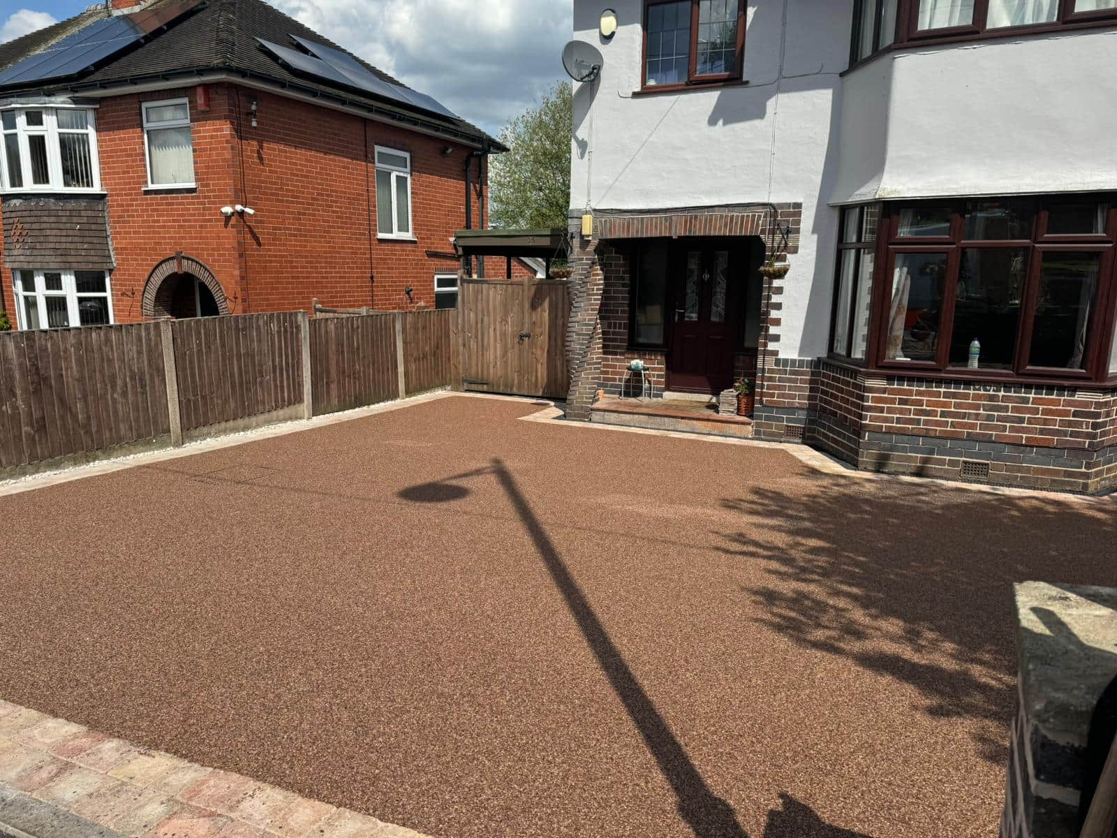 Warm-toned resin driveway outside a house with a curved lawn border