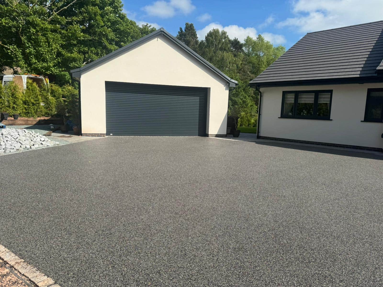 Wide grey resin driveway leading to a detached garage and home